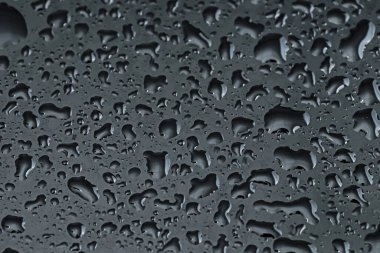 Su siyah cam yüzeyine damlıyor, yakın plan.