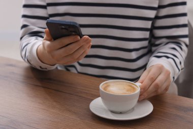 Kahve molası sırasında akıllı telefon kullanan bir kadın, kapalı masa, yakın plan.