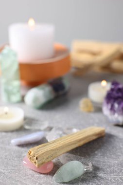 Palo Santo çubukları, değerli taşlar ve yanan mumlar açık gri masada, yakın plan.
