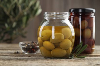 Cam kavanozlarda turşulu zeytin ve ahşap masada baharatlar, yakın plan.