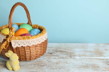 Hasır sepetteki güzel Paskalya yumurtaları ve ahşap masadaki tavşancık figürü açık mavi arkaplan, metin için alan