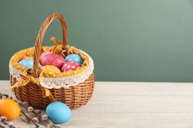 Birçok süslü Paskalya yumurtası hasır sepetinde ve söğüt dalları ahşap masa üzerinde yeşil arka planda, metin için boşluk