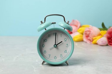 Bahar geldi. Alarm saati ve gri mermer masa üzerindeki güzel çiçekler açık mavi arkaplana karşı