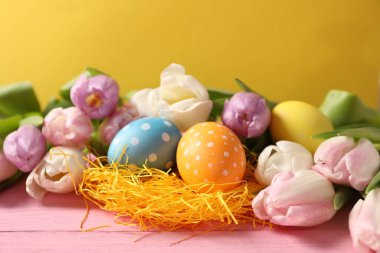 Paskalya yumurtaları ve pembe ahşap masada güzel laleler, yakın plan.
