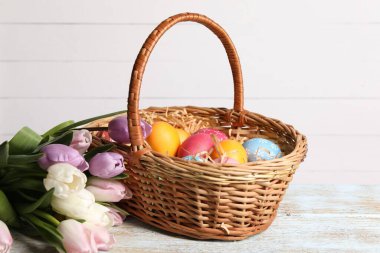 Hasır sepetteki Paskalya yumurtaları ve ahşap masada güzel laleler.