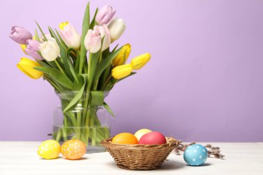 Hasır sepette paskalya yumurtaları ve beyaz ahşap masada leylak arka planda güzel laleler.