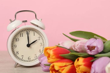 Bahar geldi. Alarm saati ve ahşap masanın üzerindeki güzel laleler pembe arka plana karşı, yakın plan.
