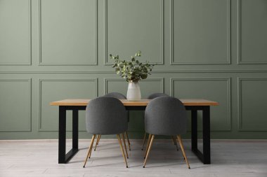 Yumuşak sandalyeler, okaliptüs dallı masa ve vazo adaçayı rengi duvarın yanındaki şık yemek odasında. İç tasarım