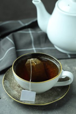 Çay poşeti sıcak içecek ve çaydanlık gri desenli masada, yakın plan.