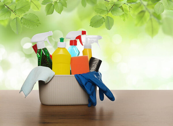 Различные чистящие средства в корзине на деревянном столе на открытом воздухе. Пространство для текста