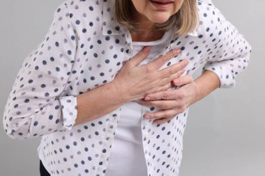 Kalp krizi geçirdi. Açık gri arka planda göğüs ağrısı çeken son sınıf öğrencisi kadın, yakın plan.