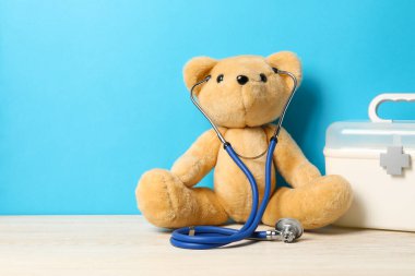 Pediatri konsepti. Steteskoplu oyuncak ayı ve ahşap masadaki ilk yardım çantası açık mavi arkaplan, metin için boşluk
