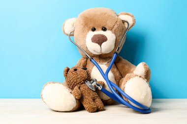 Pediatri konsepti. Ahşap masada steteskoplu oyuncak ayılar açık mavi arka planda