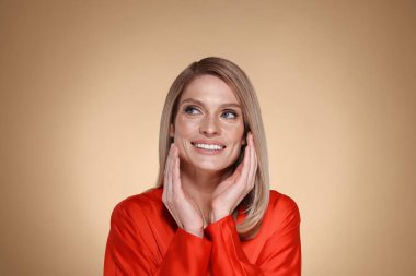 Bej arka planda düz sarı saçlı güzel mutlu bir kadının portresi.