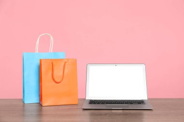 İnternet alışverişi. Laptop ve renkli kağıt torbaları pembe arka plana karşı ahşap masada.