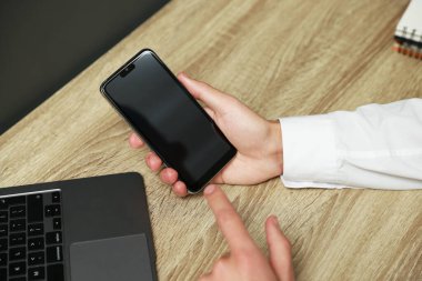 Adam ahşap masada boş ekranlı akıllı telefon kullanıyor.