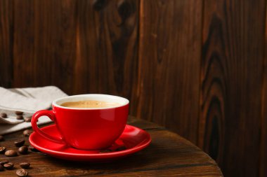 Kahveli kırmızı bardak ve ahşap masada kavrulmuş fasulye. Mesaj için yer var.