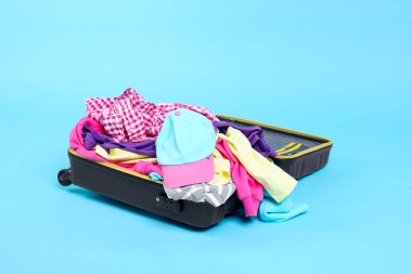 Açık mavi arka planda giysilerle dolu bavul.
