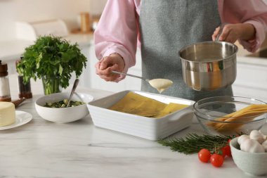 İçerideki mermer masada ıspanak lazanyasına beşamel sosu döken kadın, yakın plan.