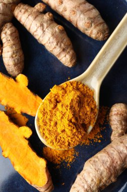 Kaşıkta aromatik zerdeçal tozu ve mavi tabakta taze kökler.