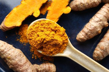 Kaşıkta aromatik zerdeçal tozu ve mavi tabakta taze kökler.