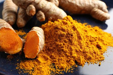 Aromatik zerdeçal tozu ve mavi tabakta taze kökler, yakın plan.