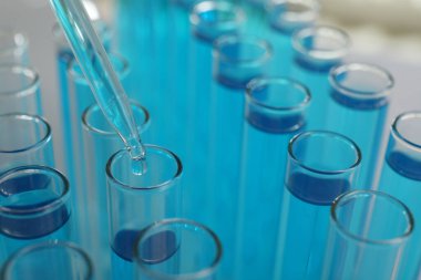 Işık arkaplanındaki test tüplerine sıvı damlatılıyor.