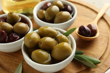 Lezzetli zeytinler tabakta, kaşık ve yeşil yapraklar masada, yakın plan.