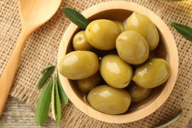 Lezzetli marine edilmiş zeytinler kasede, yeşil yapraklar ve kaşıklar masada, düz yerde.