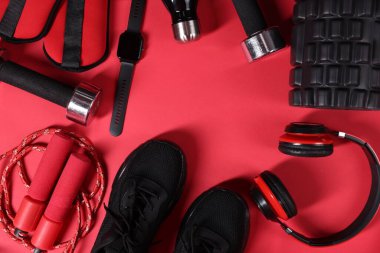 Farklı spor aletleri, kol saati ve kırmızı arka planda kulaklıklar, düz yatış. Metin için boşluk