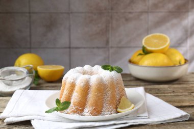 Pudra şekerli lezzetli limonlu pasta, taze meyve dilimi ve ahşap masada nane.