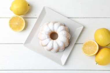 Lezzetli limonlu pasta pudra şekeri ve narenciye meyveleri beyaz ahşap masada, düz yatıyordu.