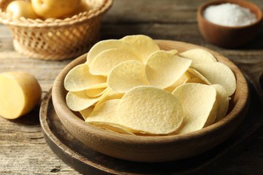 Lezzetli cips, tuz ve çiğ patatesler ahşap masada, yakın plan.