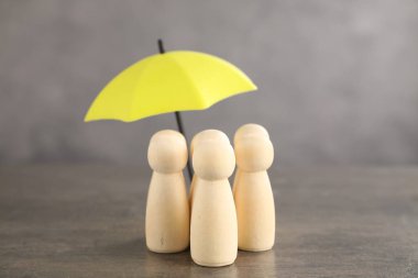 Gri masada şemsiye altındaki insan figürleri. Sigorta konsepti