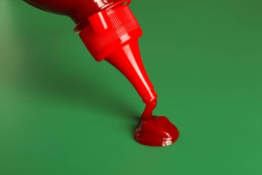 Yeşil arka planda şişeden ketçap sıkmak, yakın plan.