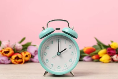 Bahar geldi. Alarm saati ve ahşap masada pembe arka planda güzel laleler.