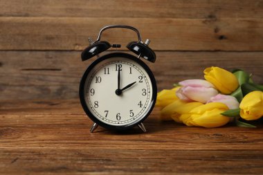 Bahar geldi. Çalar saat ve ahşap masada güzel laleler.