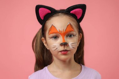 Pembe arka planda kedi gibi yüzü kulakları boyalı tatlı bir kız.