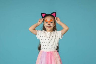 Yüzü ve kulakları açık mavi arka plandaki kedi gibi boyalı tatlı bir kız.