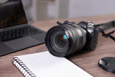 Profesyonel fotoğraf makinesi, dizüstü bilgisayar ve not defteri kapalı masa, yakın plan.