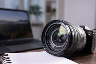 Profesyonel fotoğraf makinesi, dizüstü bilgisayar ve not defteri ahşap masada, yakın plan.