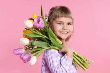 Gülümseyen küçük kız pembe arka planda bir buket laleyle