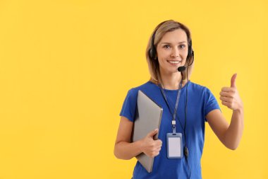 Teknik destek çağrı merkezi. Sarı arka planda dizüstü bilgisayarı olan gülümseyen operatör. Metin için boşluk