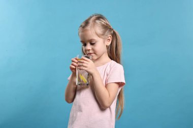 Açık mavi arka planda bir bardak limonata olan kız. Tazeleyici içecek.