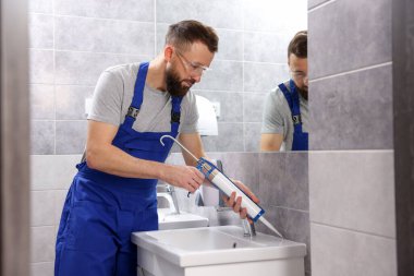 Banyodaki lavaboyu kazıma tabancasıyla mühürleyen bir işçi.