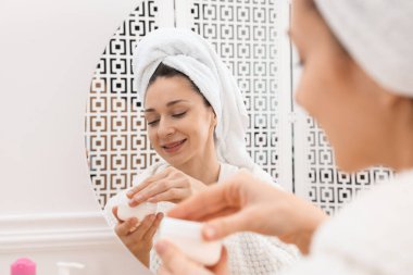 Spa günü. Kapalı alanda aynanın yanında kremalı güzel bir kadın