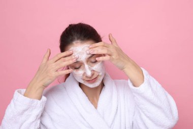 Spa günü. Güzel bir kadın pembe arka planda yüzüne maske takıyor.