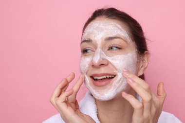 Spa günü. Güzel bir kadın pembe arka planda yüzüne maske takıyor.