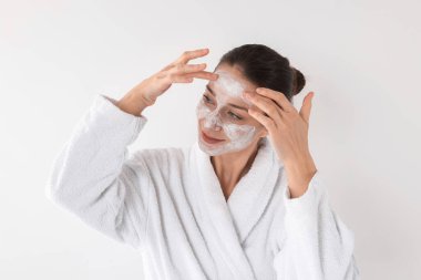 Spa günü. Güzel bir kadın beyaz arka planda yüzüne maske takıyor.
