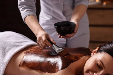 Çikolatalı vücut sargısı. Güzellik salonunda kadının sırtına maske takan bir kaplıca işçisi.